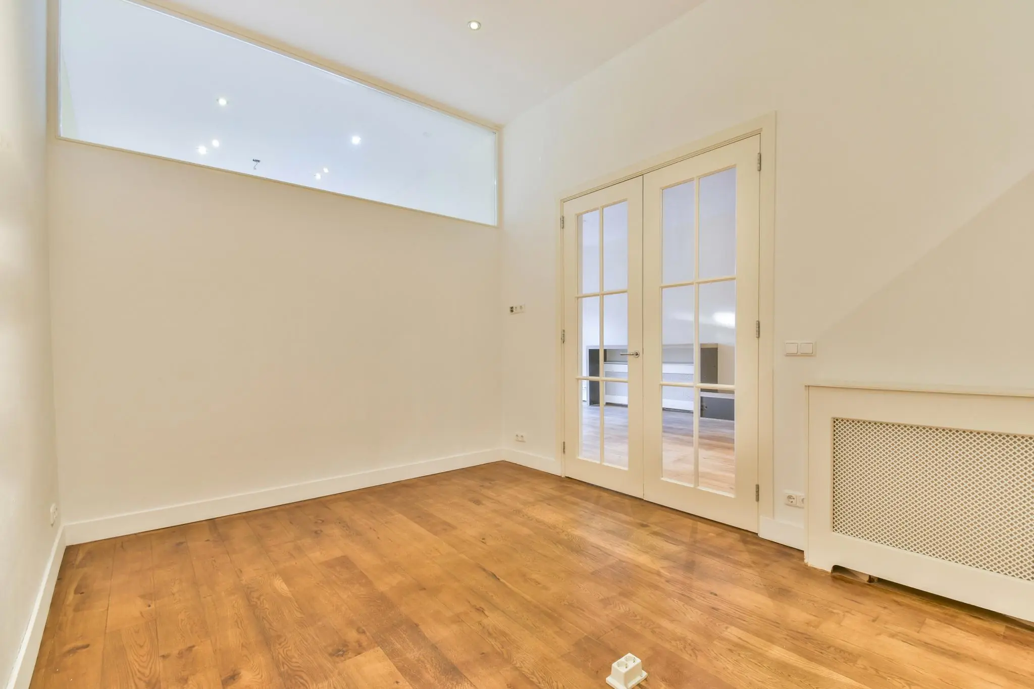 Lichte kamer met houten vloer en glazen dubbele deuren in een woning aan de Korte Schimmelstraat.